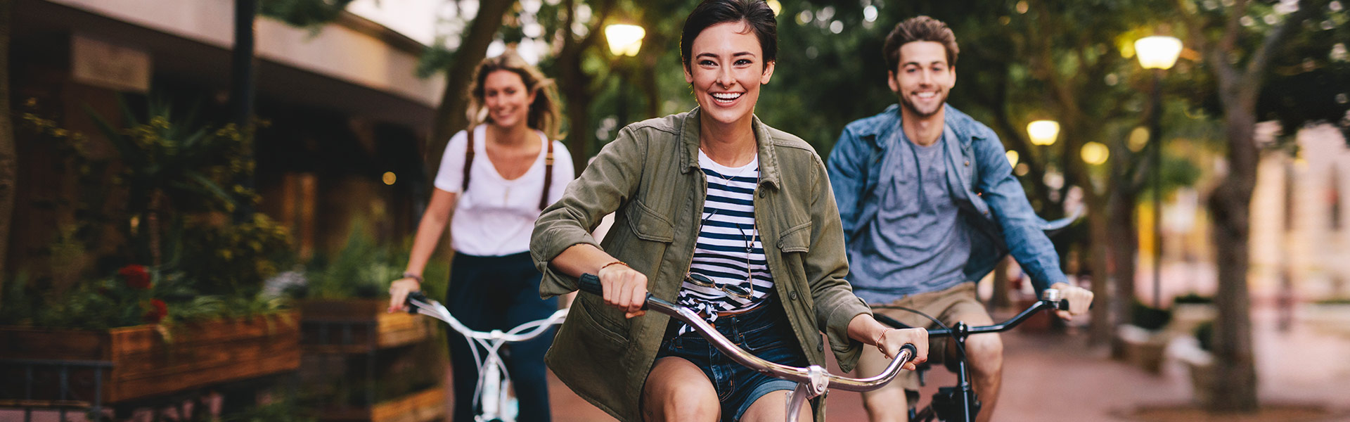 Three young smiling friends riding bikes down the sidewalk