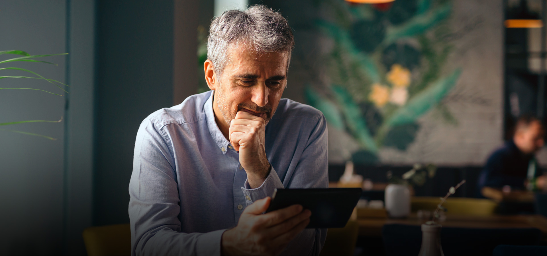 Older gentleman sitting at a table in a restaurant looking at a tablet